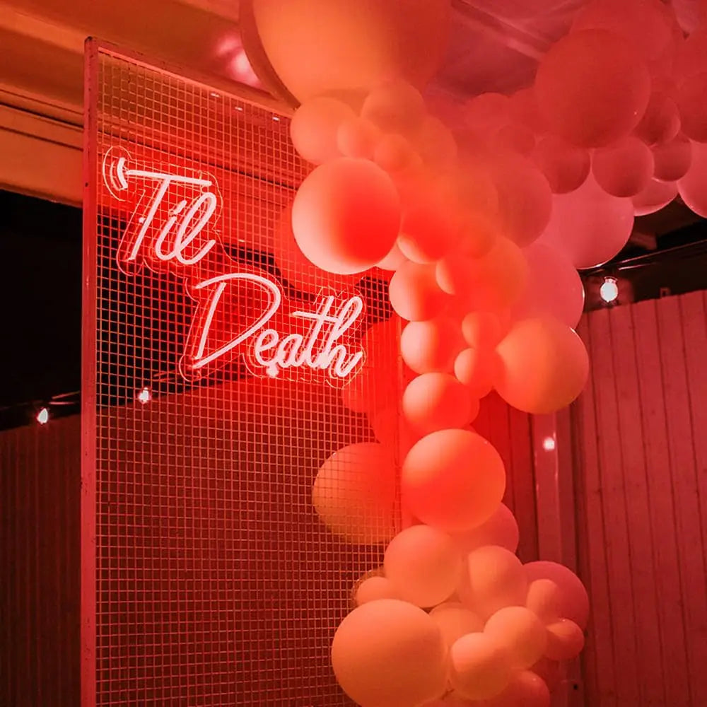 Neon sign with 'Til Death' surrounded by balloons in a romantic setting